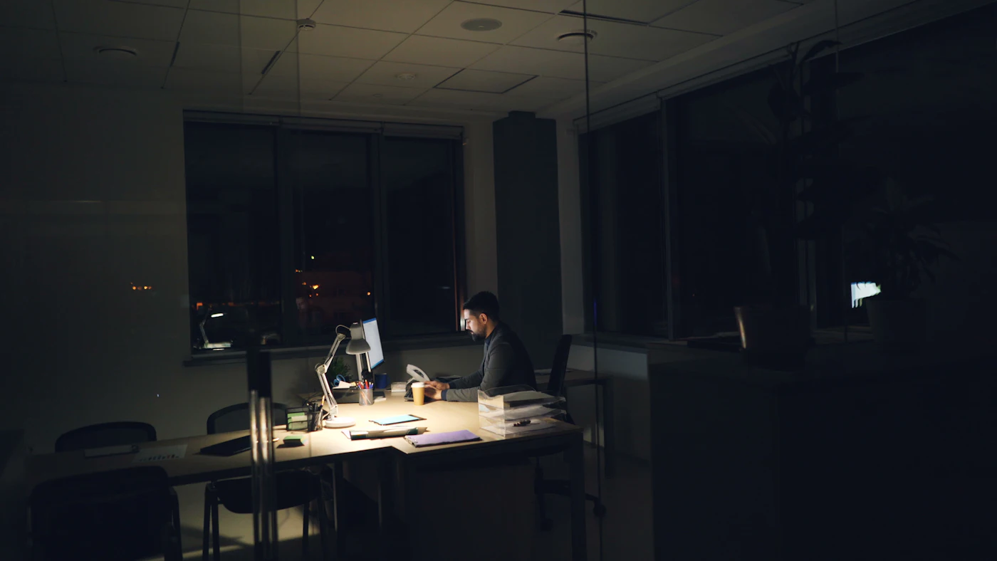Empresário trabalhando sozinho em um escritório escuro, iluminado apenas pela luz da mesa.